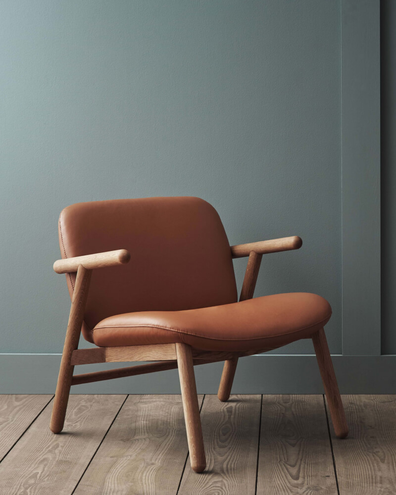 Turned oak lounge chair with cognac leather upholstery against muted sage wall