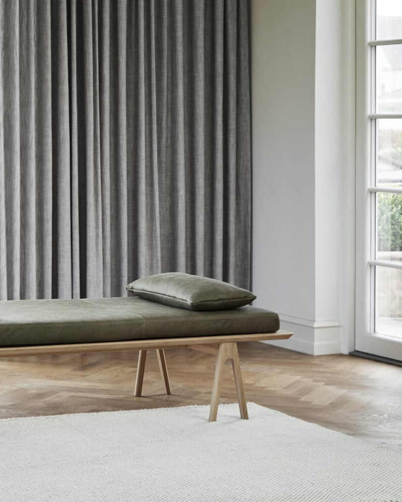 Sculptural solid oak daybed upholstered in olive leather with full-height linen drapery