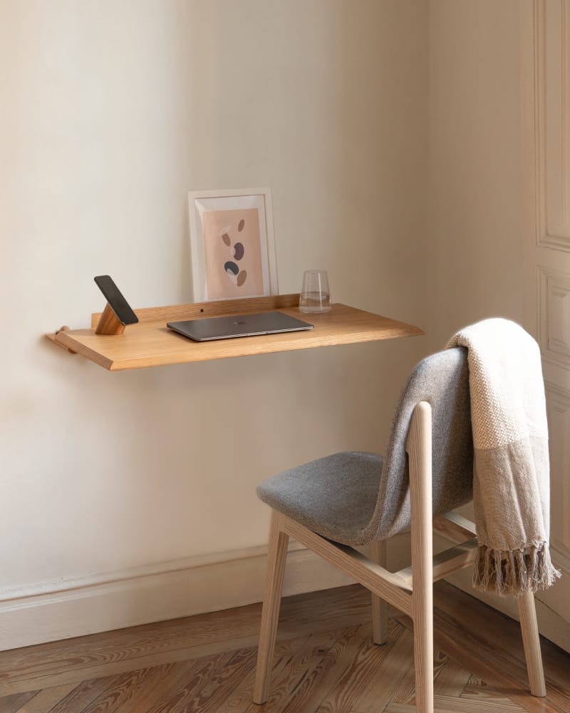 Cantilevered solid oak wall desk with upholstered timber chair, wool throw, and framed print against warm ivory wall