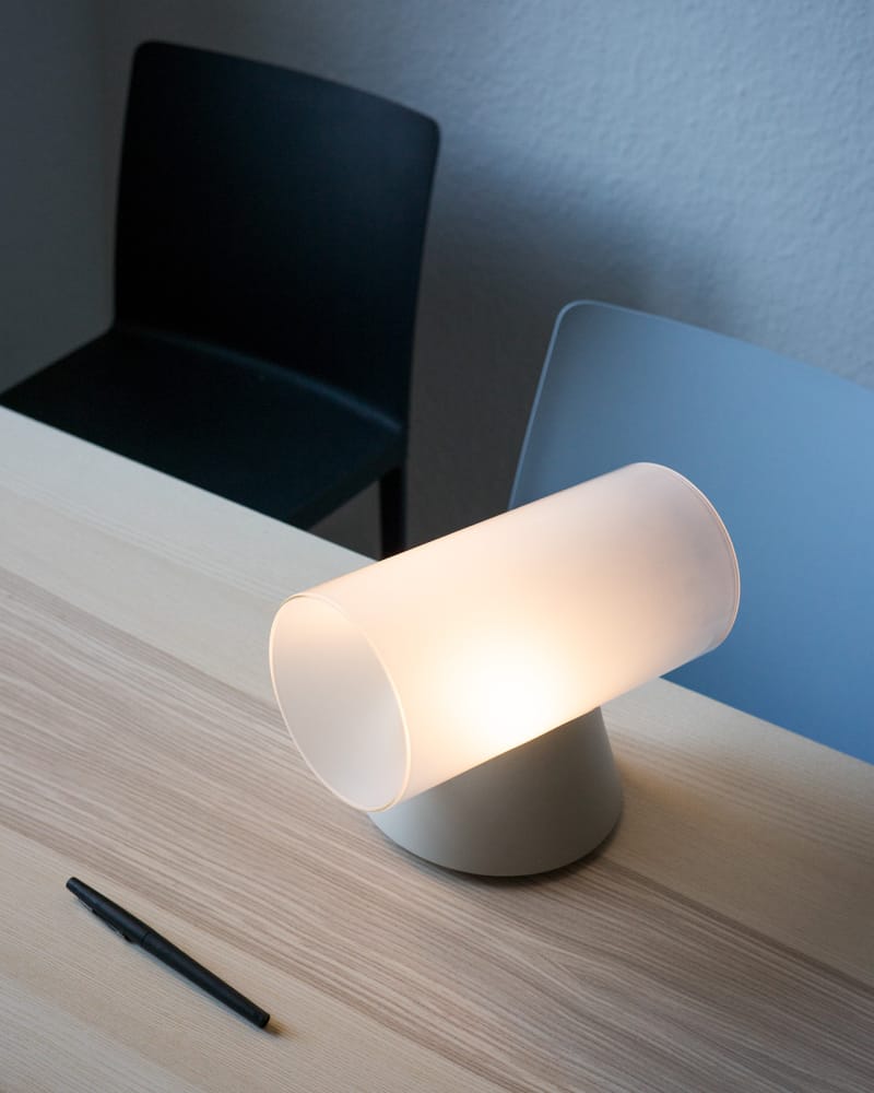 Frosted glass cylinder desk lamp resting on a pale timber worktable
